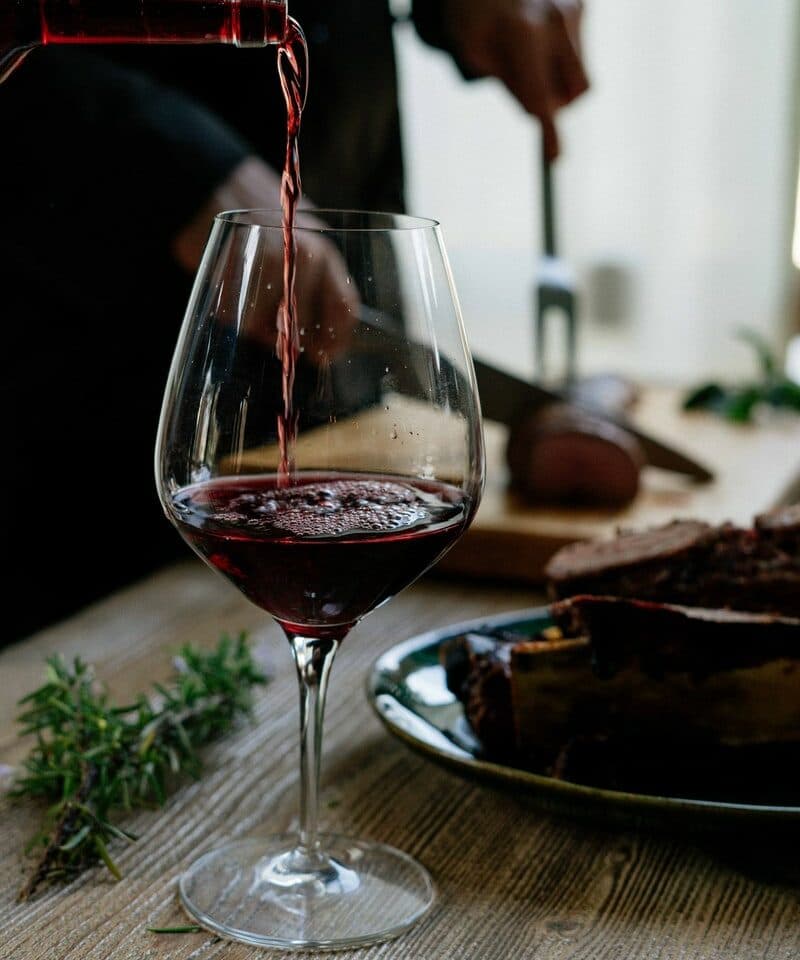 person pouring red wine on wine glass